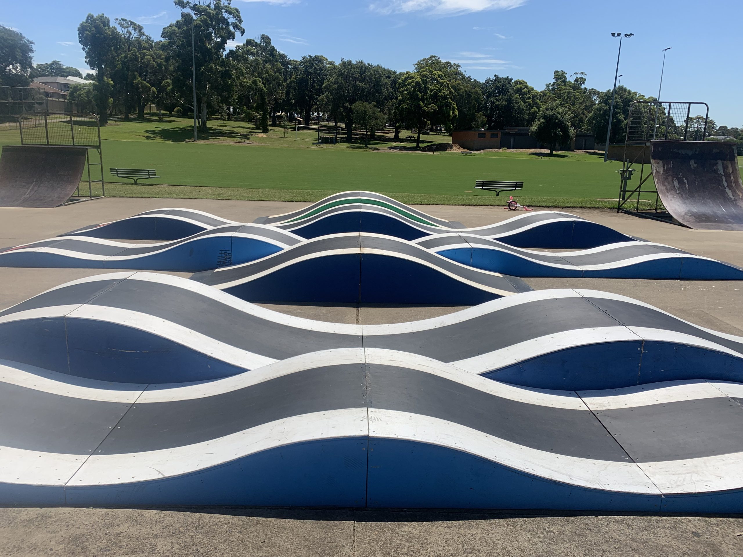 Custom pump track (skateboard ramp) in blue, black and white at a park.