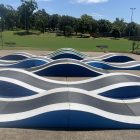Custom pump track (sktaeboard ramp) in blue, black and white in a park.