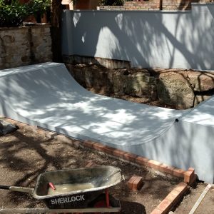 2.5ft high mini ramp - (half pipe skateboard ramp), painted grey with custom landscaping.