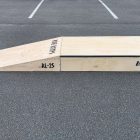 25cm high launch ramp - grind pad combo (wedge skateboard ramp plus manual pad-grind box) in raw timber, side view.